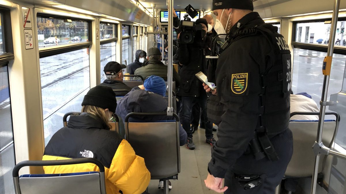 ÖPNV bleibt sicher: Während einer 3 G Kontrolle steht ein Polizist in einer Straßenbahn neben Kunden