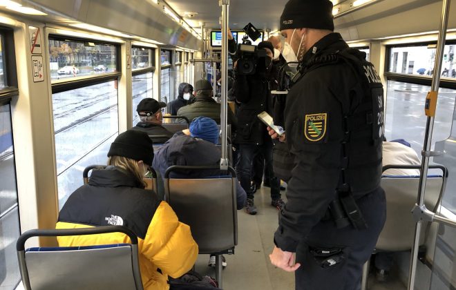 ÖPNV bleibt sicher: Während einer 3 G Kontrolle steht ein Polizist in einer Straßenbahn neben Kunden